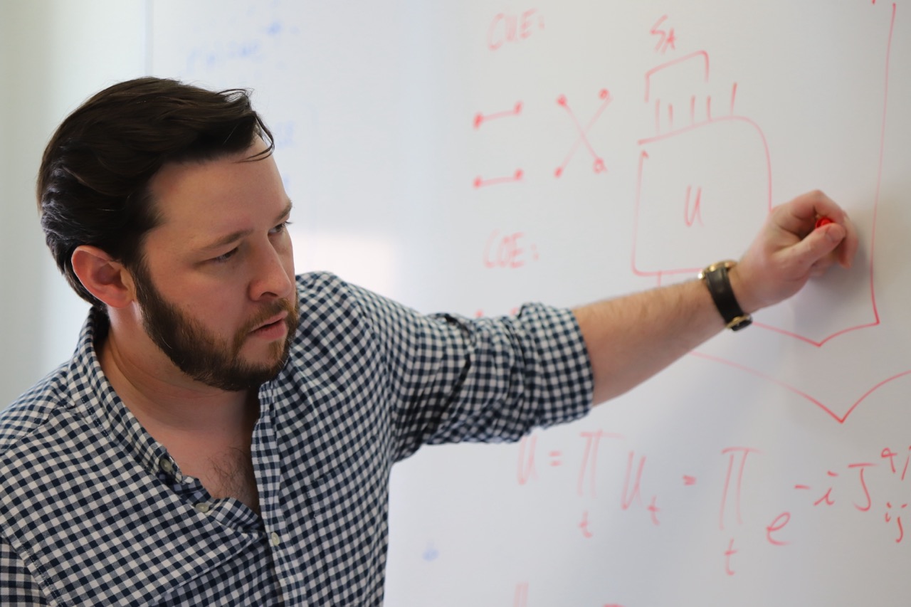 Gregory Bentsen writing quantum circuit notation on a whiteboard